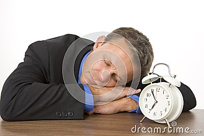 Businessman Asleep On Desk By An Alarm Clock Stock Photo