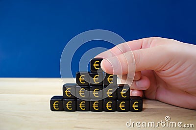 Businessman assembling black dices with gold â‚¬ euro signs in a shape of pyramid in a conceptual image Stock Photo