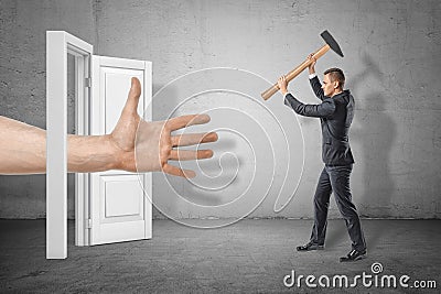 Businessman with axe in hands on the right ready to hit huge human hand reaching out through white doorway on the left. Stock Photo