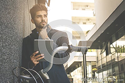 Businessman with bike leaning on wall and holding digita Stock Photo