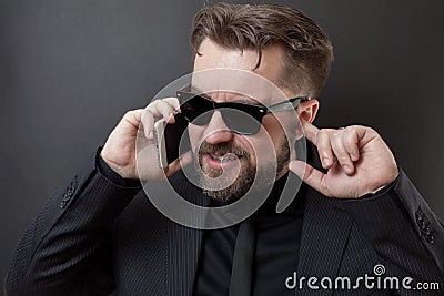 A businessman in a black suit and glasses is talking on the phone. He does not hear his interlocutor, so he plugs his free ear wit Stock Photo