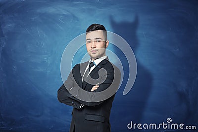 Businessman on blue chalkboard background with his shadow having devil horns. Stock Photo