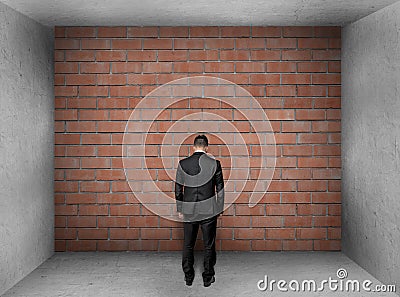 Businessman with bowed head stands front of a brick wall in interior. Stock Photo