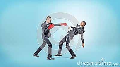 A businessman in boxing gloves fails to punch another man who manages to avoid the kick. Stock Photo