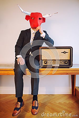 Businessman with a bull head mask sitting next to vintage radio Stock Photo