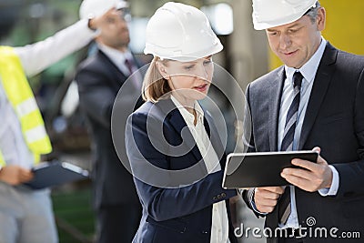 Businessman and businesswoman using digital tablet with colleagues in background at industry Stock Photo