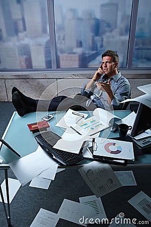 Businessman on call feet up papers all around Stock Photo