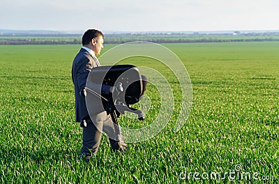 Businessman carries an office chair in a field to work, freelance and business concept, green grass and blue sky as background Stock Photo