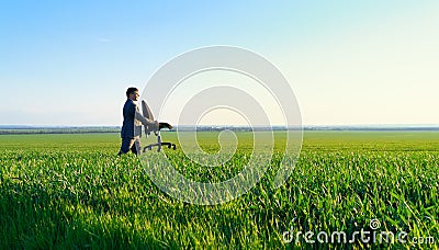 Businessman carries an office chair in a field to work, freelance and business concept, green grass and blue sky as background Stock Photo