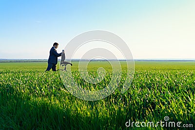 Businessman carries an office chair in a field to work, freelance and business concept, green grass and blue sky as background Stock Photo