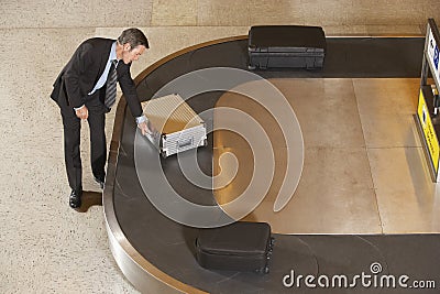 Businessman Claiming Suitcase At Luggage Carousel In Airport Stock Photo