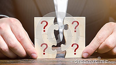 Businessman collects puzzles with question marks. Asking questions, searching for truth. Riddle mystery, investigation and Stock Photo