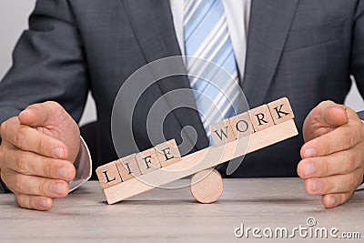 Businessman covering imbalance between life and work on seesaw Stock Photo