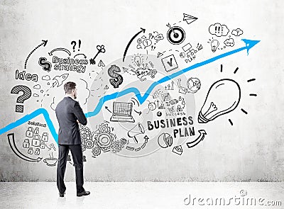 Businessman in a dark suit looking at a concrete wall with a growing blue graph and business plan icons depicted on it. Stock Photo
