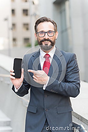 Businessman and digital gadget. Portrait of smiling businessman pointing finger at blank screen mobile phone Stock Photo