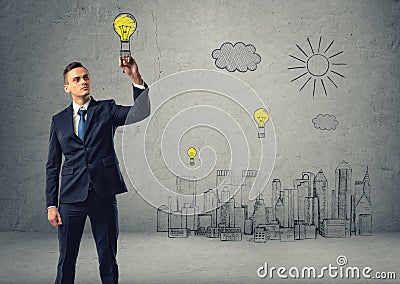 Businessman draws bulb-parachute over sketch of city. Stock Photo