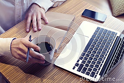 Businessman drinking coffee and working on laptop computer, mobile phone, writing business plan, wearing white shirt Stock Photo