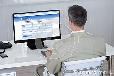 Businessman Filling Survey Form On Computer At Desk Stock Photo