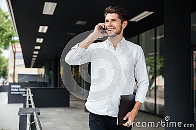 Businessman with folder talking on cell phone near business center Stock Photo