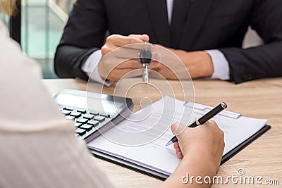 Businessman giving house keys and customer signing loan agreement document with calculator on wooden desk. Stock Photo