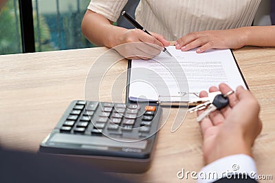 Businessman giving key and customer signing loan agreement document with calculator on wooden desk. Stock Photo
