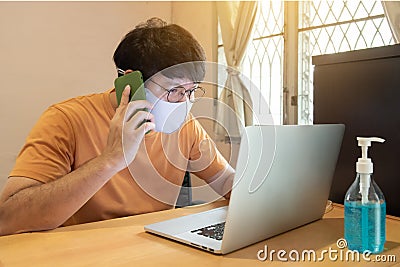 Businessman with glasses in casual dress talking by mobile phone, working on laptop computers at home, idea for coronavirus crisis Stock Photo