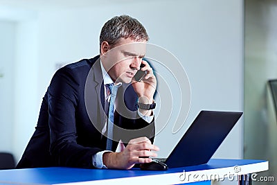 Businessman gray in a suit talking on the phone in front of laptop. Stock Photo