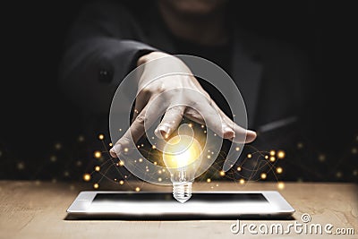 Businessman hand cover on lightbulb glowing with orange light on tablet. Creating and idea concept Stock Photo