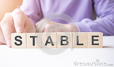 Businessman hand holding wooden cube block with STABLE business word on table background Stock Photo