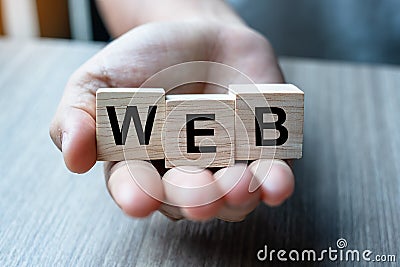 Businessman hand holding wooden cube block with WEB business word on table background. website, network, Database, and marketing Stock Photo