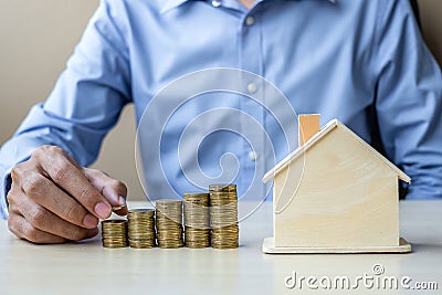 Businessman hand putting golden coin on growing money stairs or stack with house model. business, investment, retirement planning Stock Photo