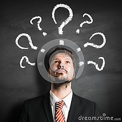 Businessman having many questions symbolized as questionmarks on a blackboard Stock Photo