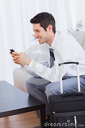 Businessman with his suitcase using mobile phone smiling Stock Photo
