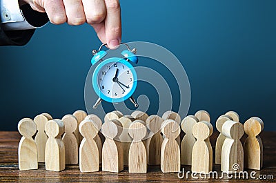 A businessman is holding an alarm clock over a crowd of people. Time management. Hourly wages, strict work limits and time Stock Photo