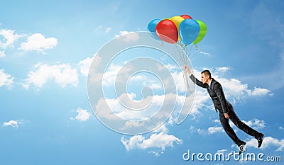 A businessman holding a batch of colorful balloons that let him fly through the clouds. Stock Photo