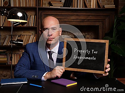 Businessman holding a chalkboard. Business concept about Property Tax Assessments with phrase on the sheet Stock Photo