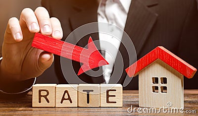 Businessman holding the down arrow on wooden blocks with the word Rate and house. Low interest in mortgages. Reducing interest Stock Photo