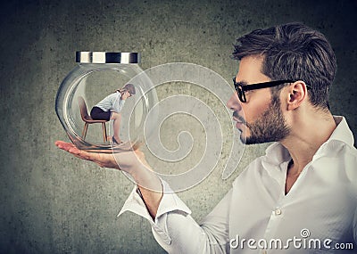 Business man holding a glass jar with a young sad business woman trapped in it Stock Photo