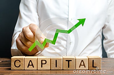 A businessman is holding a green up arrow above the word Capital. Increasing the attractiveness of the conditions for business Stock Photo
