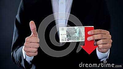 Businessman holding russian ruble banknotes showing thumbs up, arrow falling Stock Photo