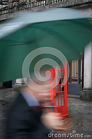 Businessman holding an umbrella in a hurry passing a red telephone box Stock Photo