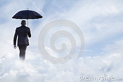 Businessman holding an umbrella and walking away in dreamlike clouds Stock Photo