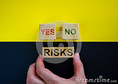 Businessman holds a block with word `risks`. Wooden cubes with words `yes, no`. Beautiful yellow and black background. Copy s Stock Photo