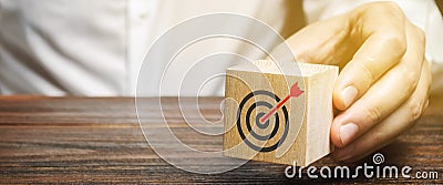 A businessman holds in his hands a wooden block with a target symbol. The concept of achieving business goals. Execution of a Stock Photo