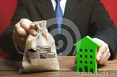 Businessman holds a money bag near a wooden house. Real estate investing concept. Developer. Taxes, mortgage, loan. Planning and Stock Photo