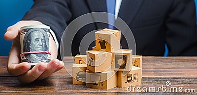 Businessman holds out a bundle of dollars near a pile of boxes. Profit, Superprofits. Investments financing in production, taxes Stock Photo