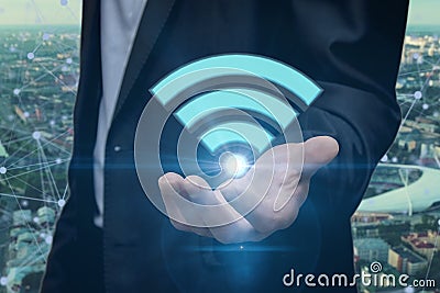 A businessman holds a shining Wi-Fi icon against the city background. Concept: free Internet connection, unlimited traffic, networ Stock Photo