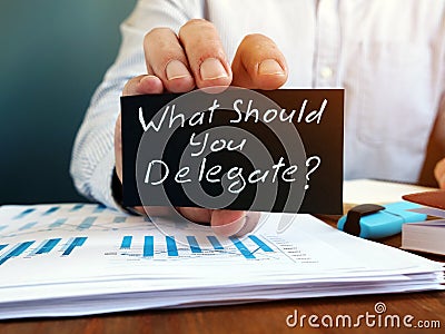Businessman holds sign What Should You Delegate. Delegation concept Stock Photo