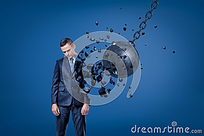 Businessman looking down, hands at sides, being destroyed in pieces by demolition ball. Stock Photo