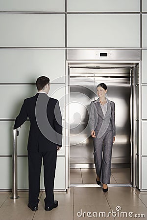 Businessman Looking At Female Colleague Exiting Elevator Stock Photo